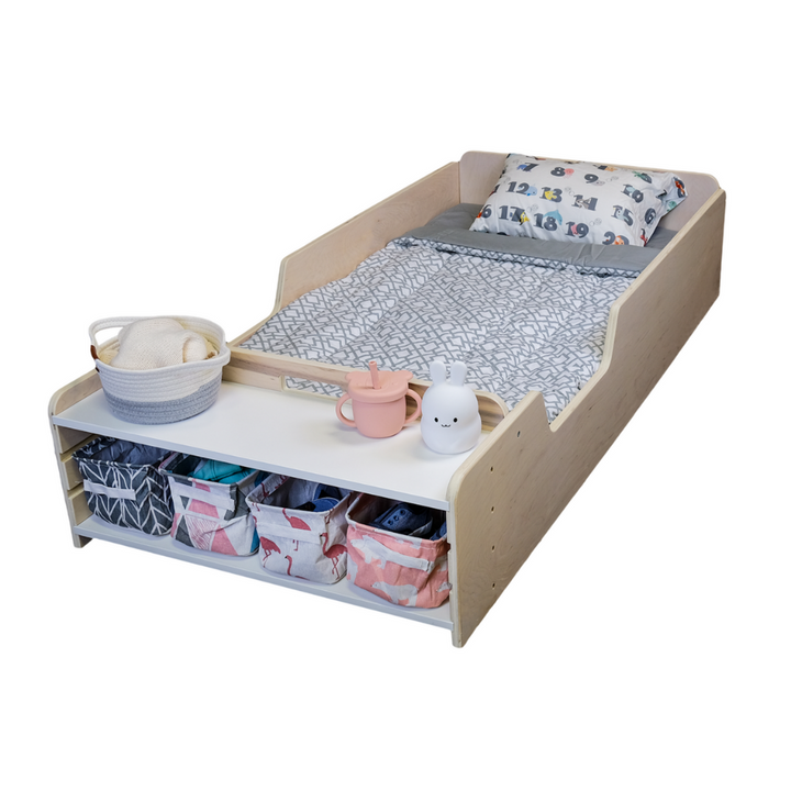 A Montessori Floor Bed with rails and storage shelves, equipped with a mattress, pillows, and storage bins, placed in a home environment.