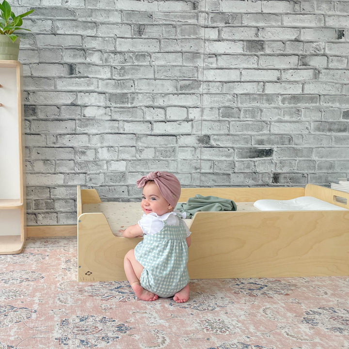 Baby sitting on a wooden floor with a brick-patterned wall in the background