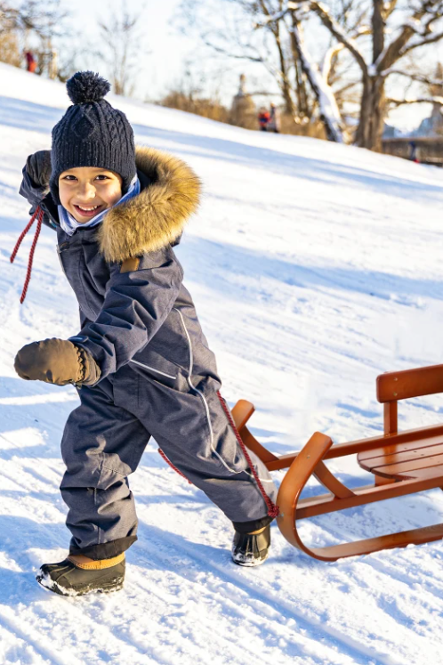 Child in winter clothing with a sled on a snow-covered hill