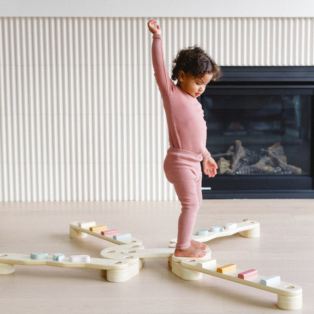 Child standing on a wooden balance board in a home setting