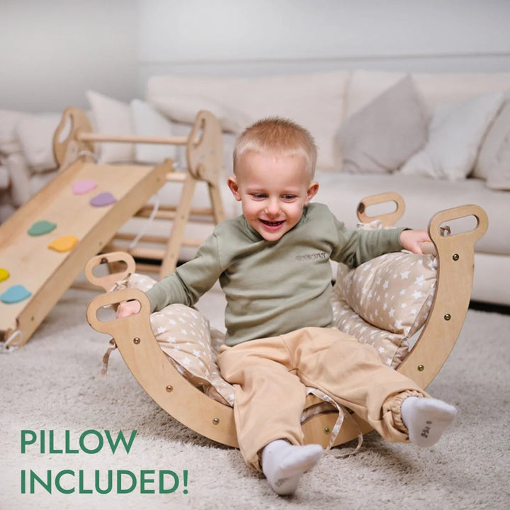 Child sitting on a wooden rocking chair with a pillow, smiling in a room with a slide and couch.