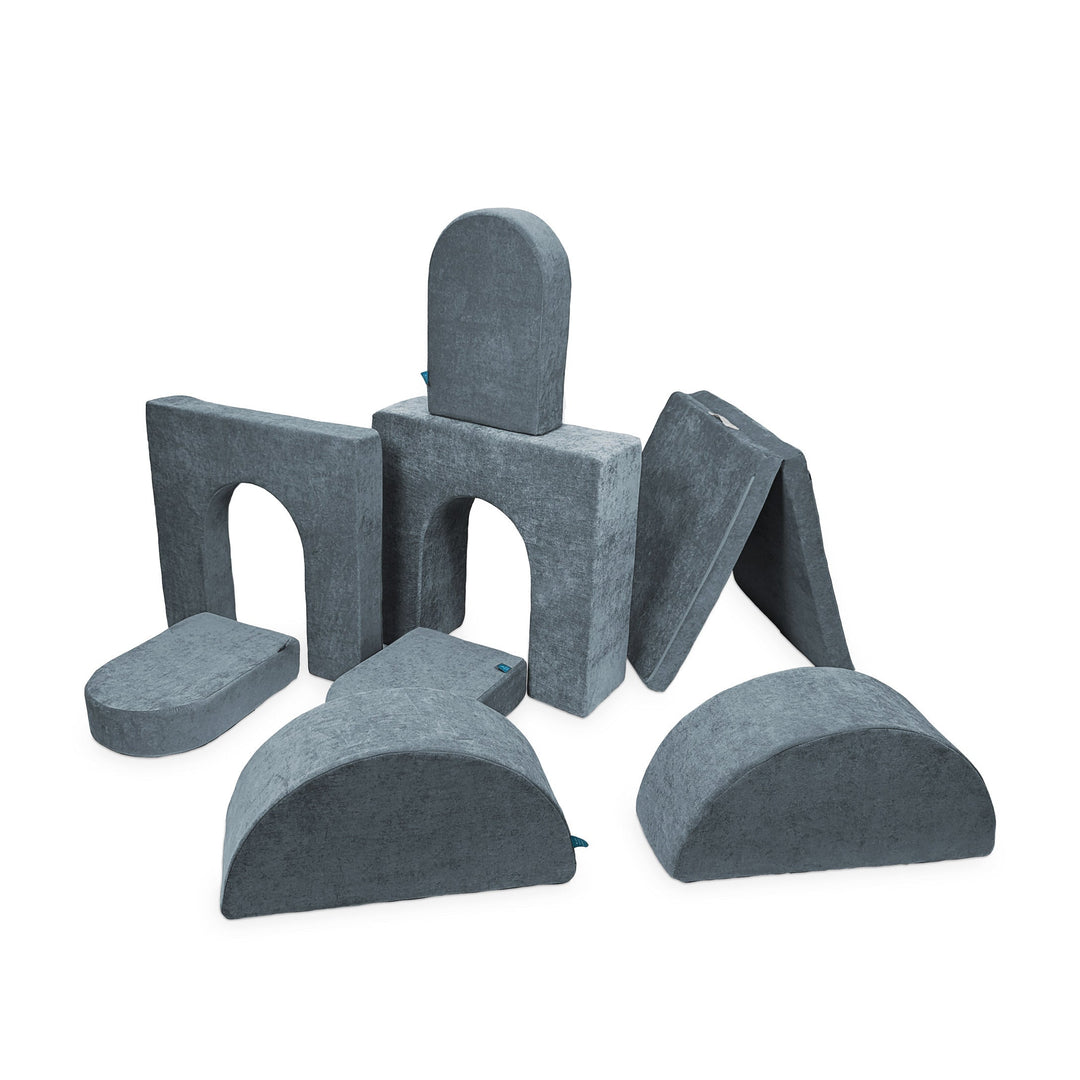 A set of gray modular foam pieces designed for creative play, including arches, steps, and other shapes.