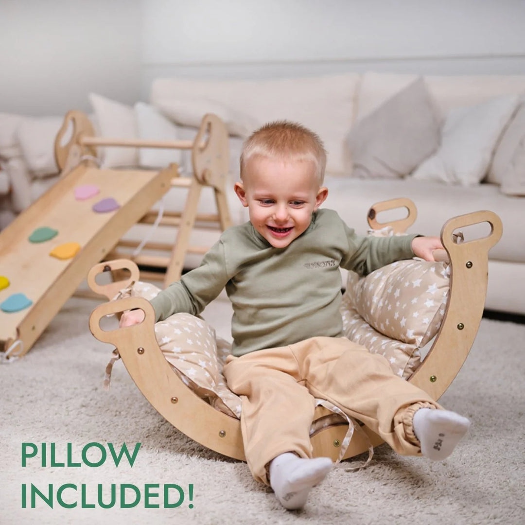 Child sitting on a wooden rocking chair with a pillow, smiling in a room with a slide and couch.